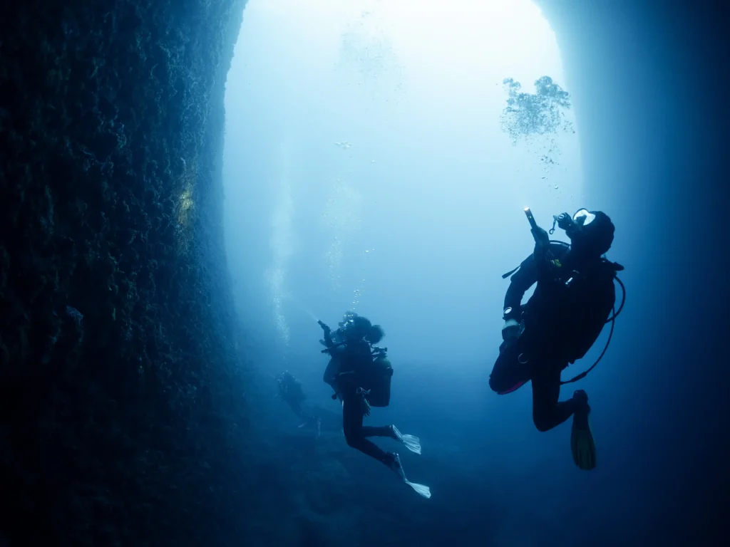 scuba-divers-with-flashlight-swimming-in-dark-cave